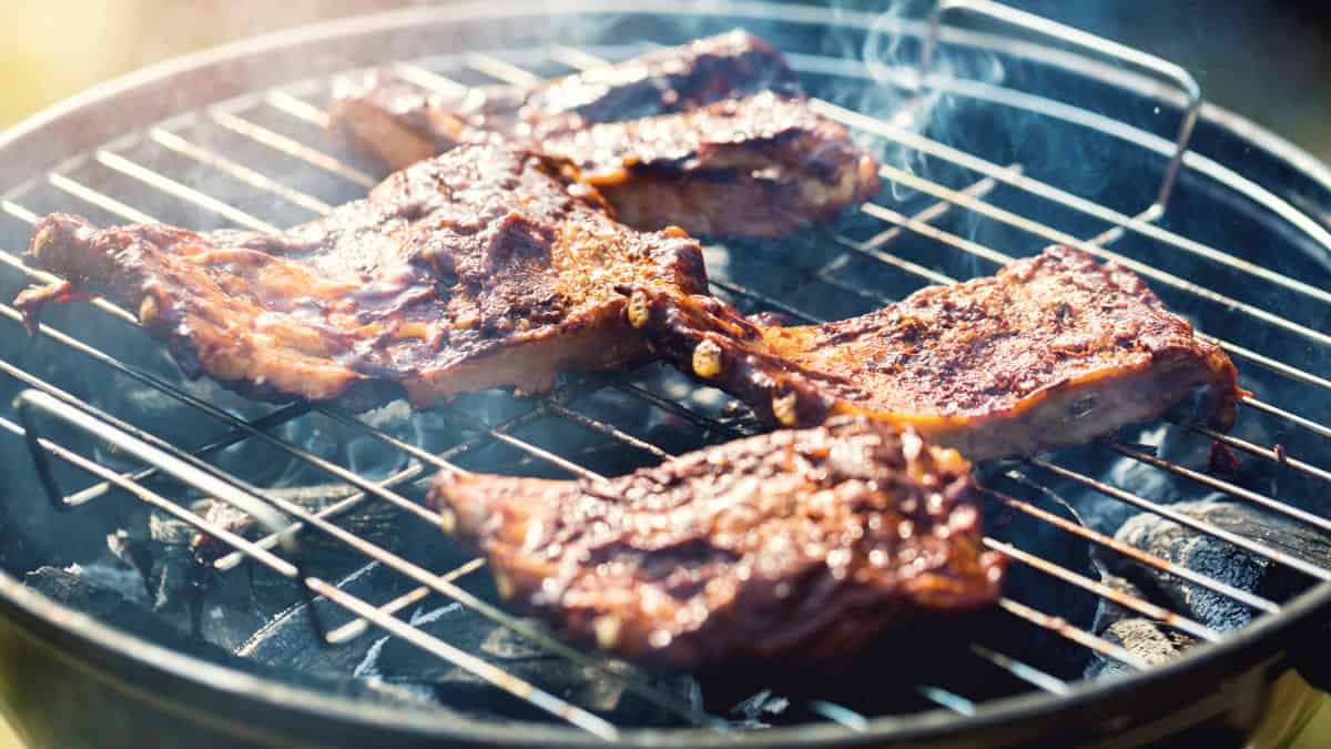 Close up of meat being grilled on a round charcoal grill with lid off