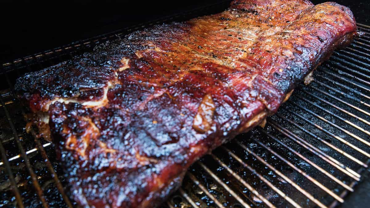 A rack of ribs in a pellet smoker with thermometer probe in