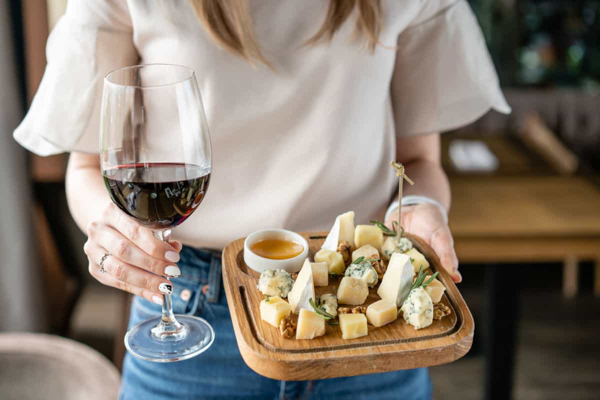 A woman carrying a cheese board and a glass of wine