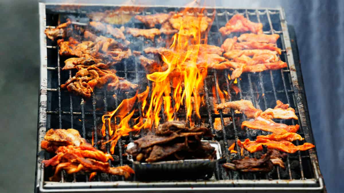 A grill flaring up with pieces of chicken on the grate