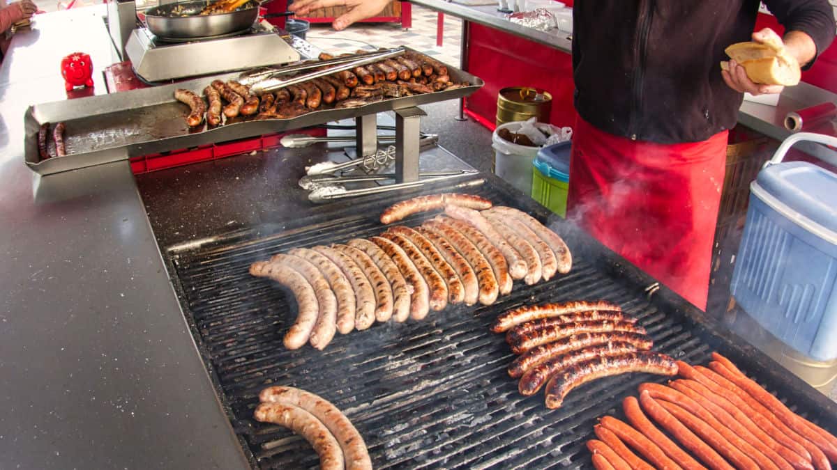 Brats and sausages being grilled on a large charcoal grill
