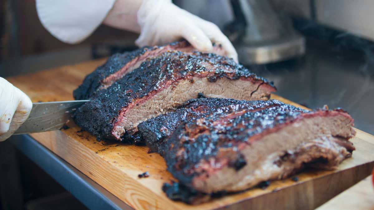 Man in white gloves slicing a smoked brisket