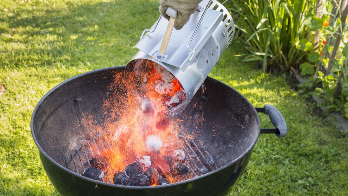 A charcoal chimney of hot coals being poured into a charcoal grill