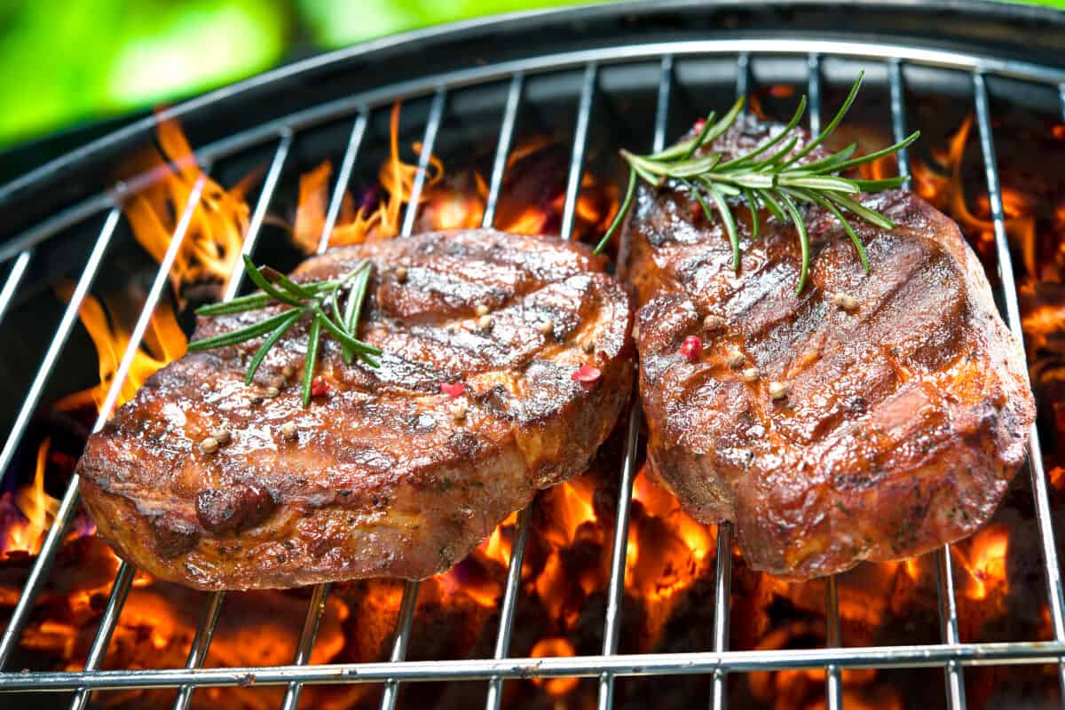 Two steaks with sprigs of rosemary on a charcoal grill