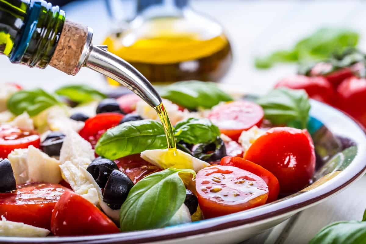 Close up of a dressing being poured over a brightly colored salad of tomatoes, cheese and basil