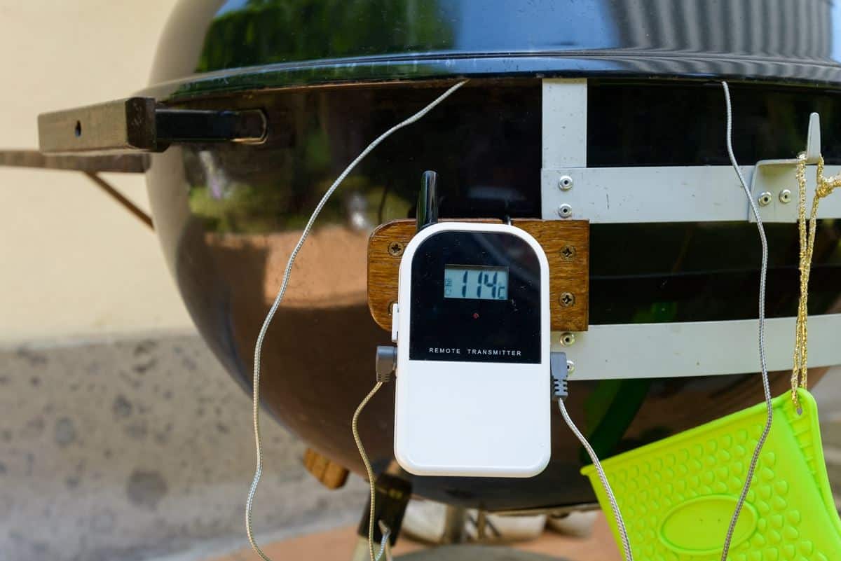 A white smoker thermometer transmitter clipped to the leg of a grill