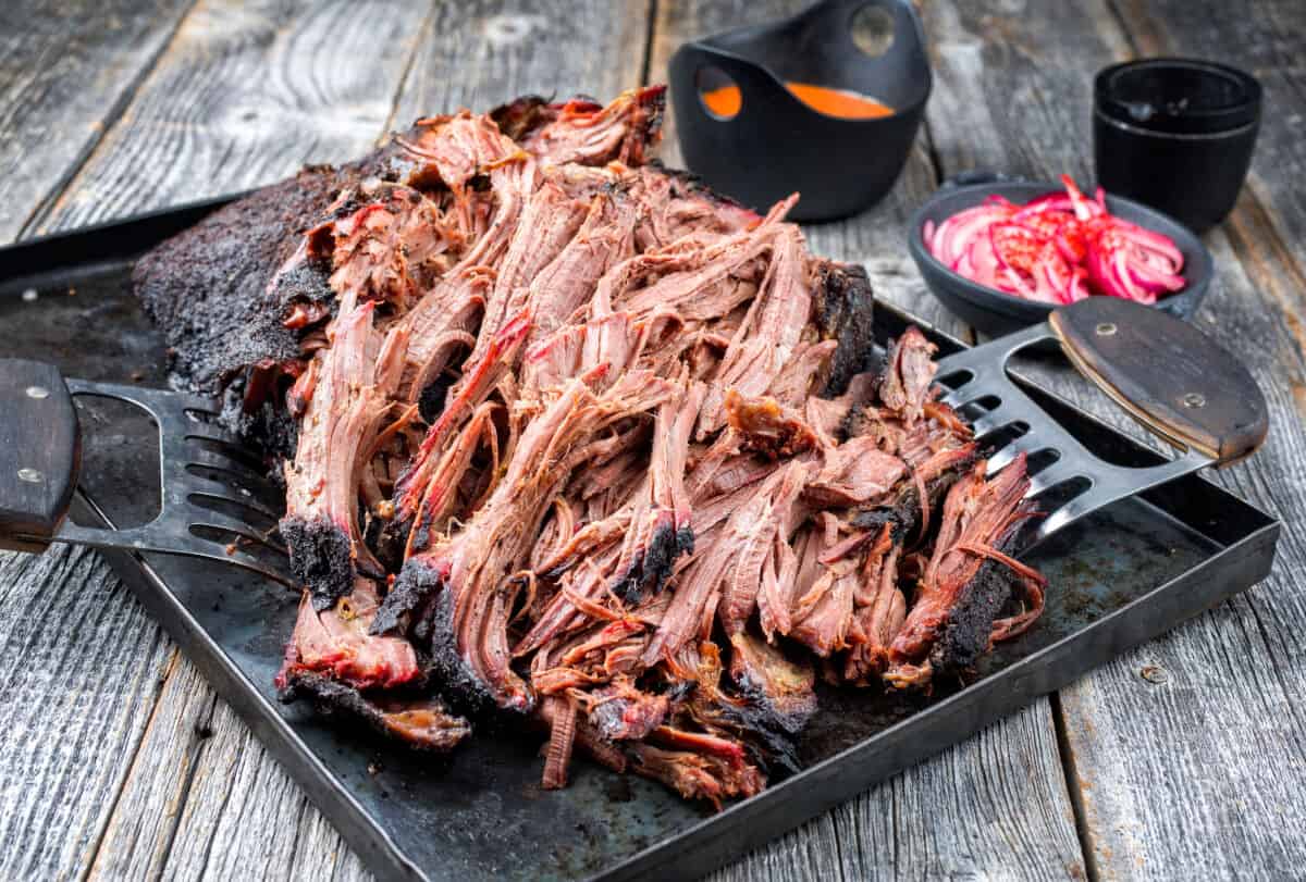 pulled pork on a dark cutting board with some meat shredding claws