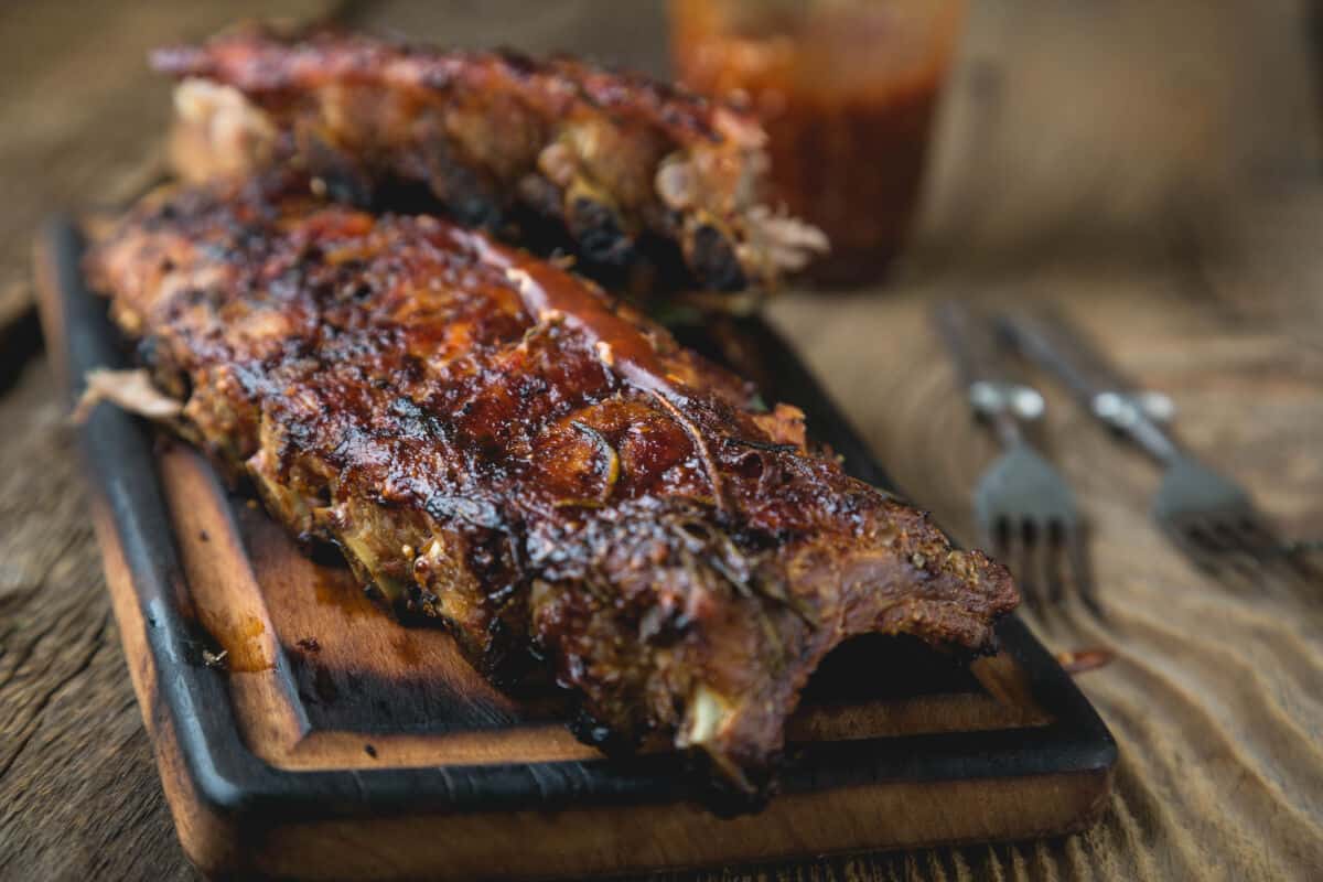 A rack of barbecue pork ribs on a slightly charred wooden cutting board