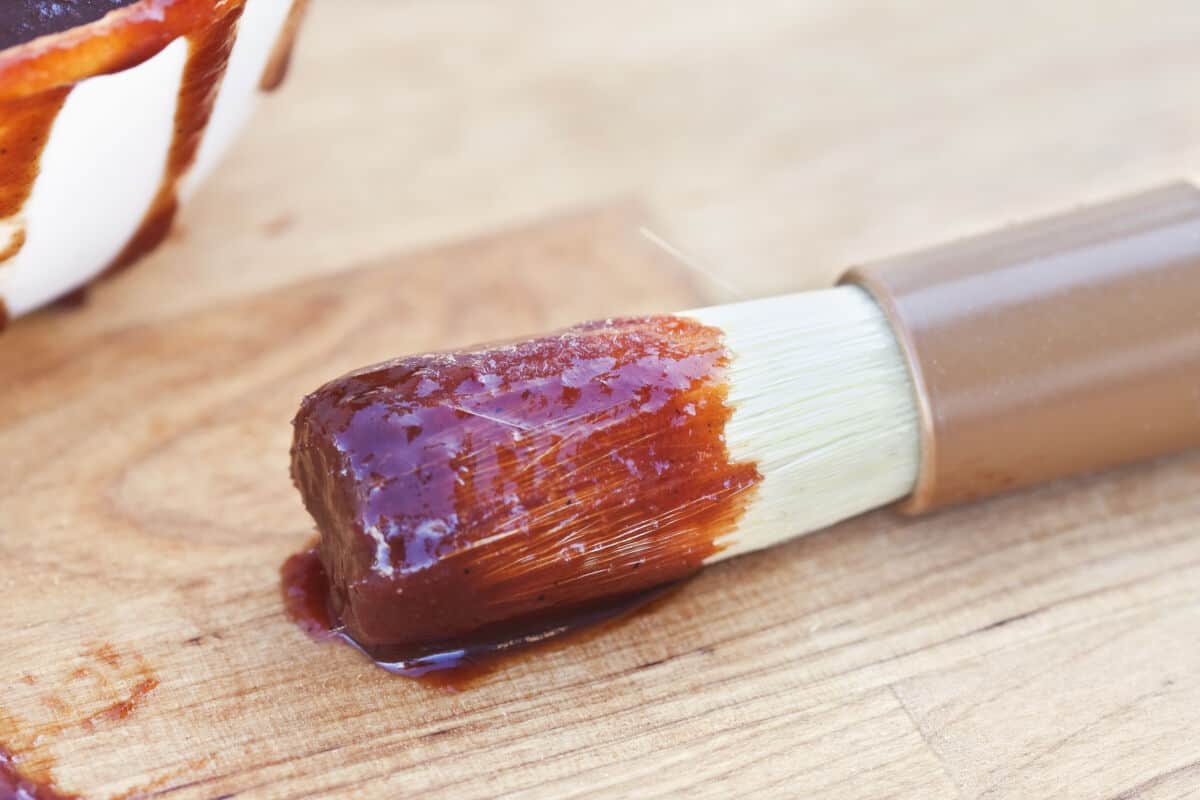 a basting brush with sauce on the end, sitting on a wooden table