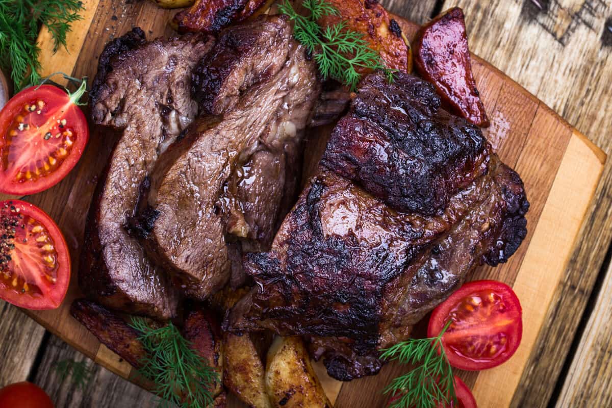 A smoke roasted and sliced chuck roast surrounded by veg and some herbs