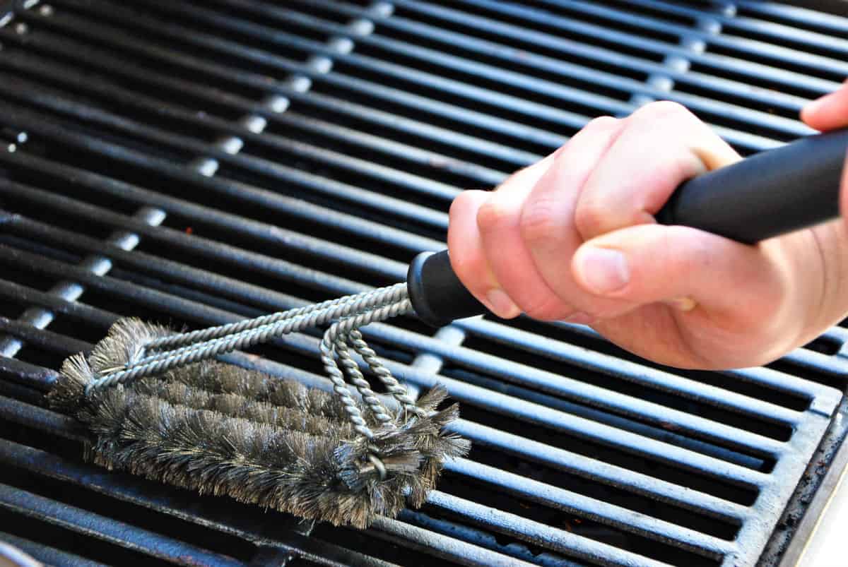 A grill brush being used on some grates