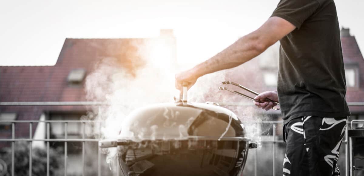 A man removing the lid form a heavily smoking grill