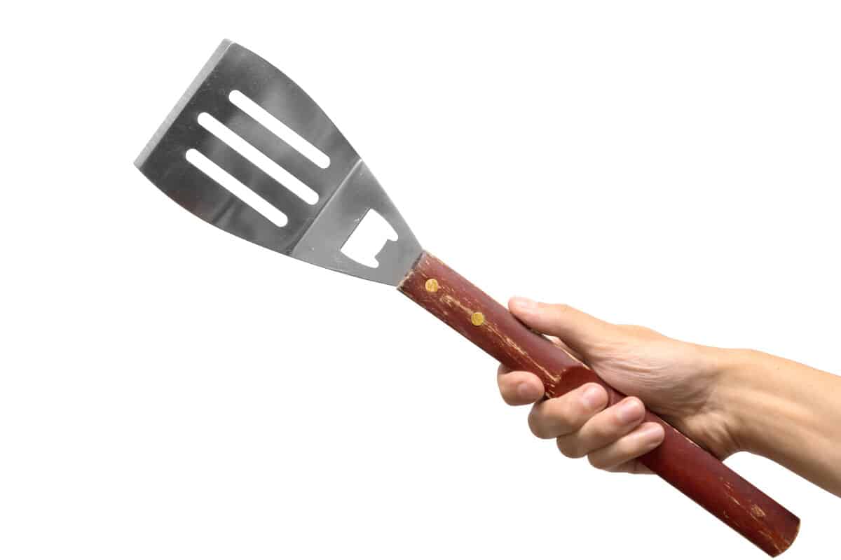 A hand holding a grilling spatula isolated on white