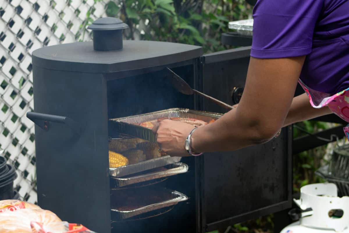 A cabinet style smoker being loaded with meat by a man