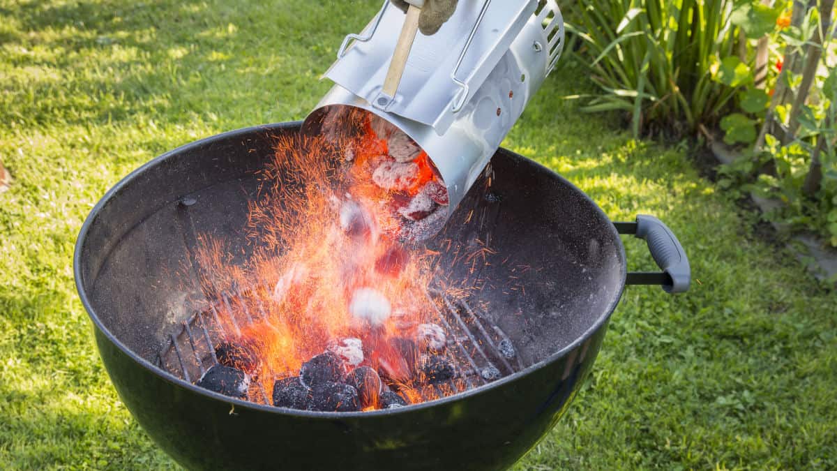 A charcoal chimney starter being poured out into a kettle grill