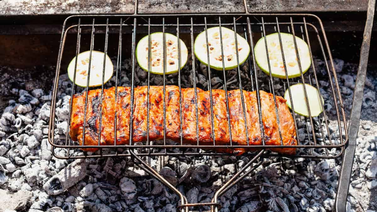 A grill basket over charcoal with ribs and courgette slices