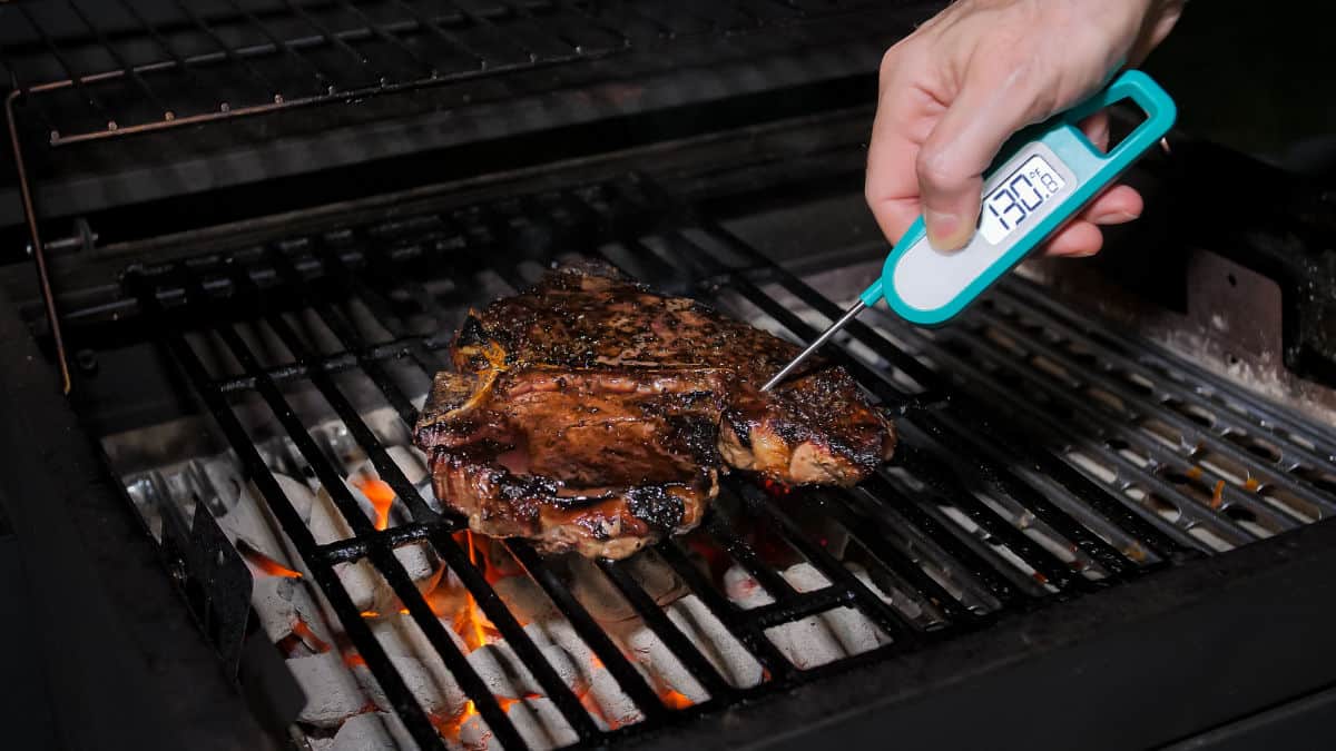 A blue and white instant read thermometer taking the internal temperature of meat