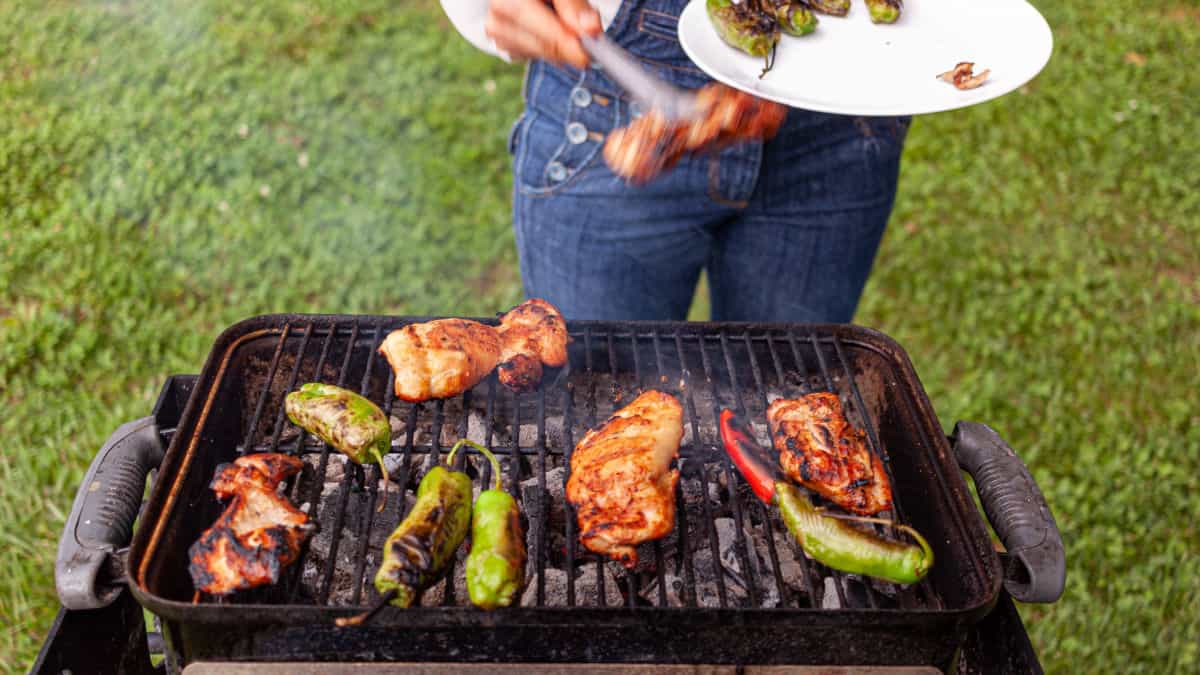 Weber go anywhere grill cooking meat and peppers, with a someone helping themselves to food