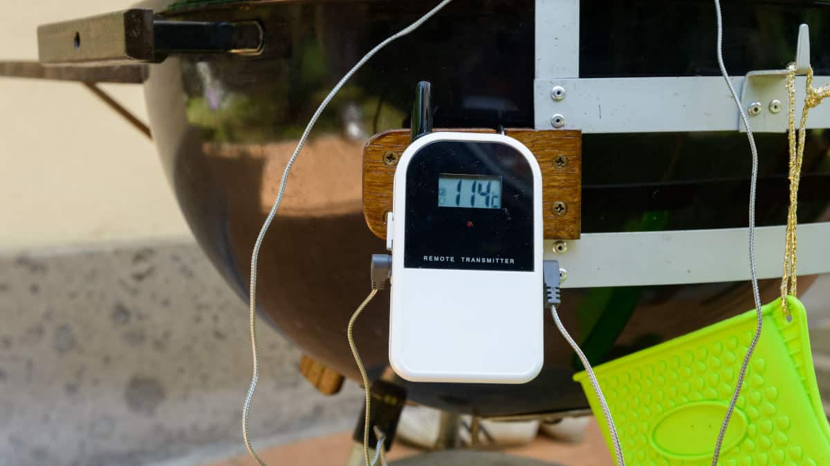 A wireless meat thermometer transmitter on the leg of a kettle grill and smoker
