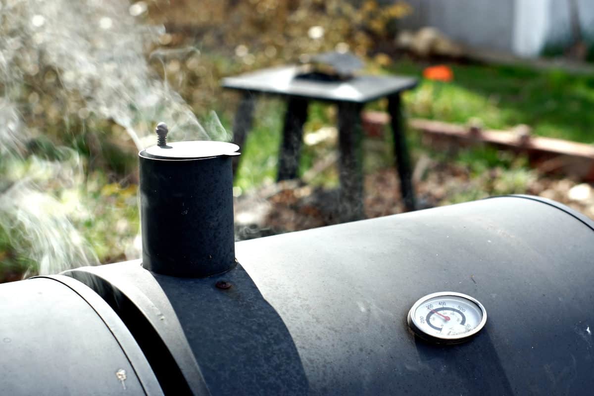 A barrel type smoker, with chimney, and a thin wisp of smoke coming out