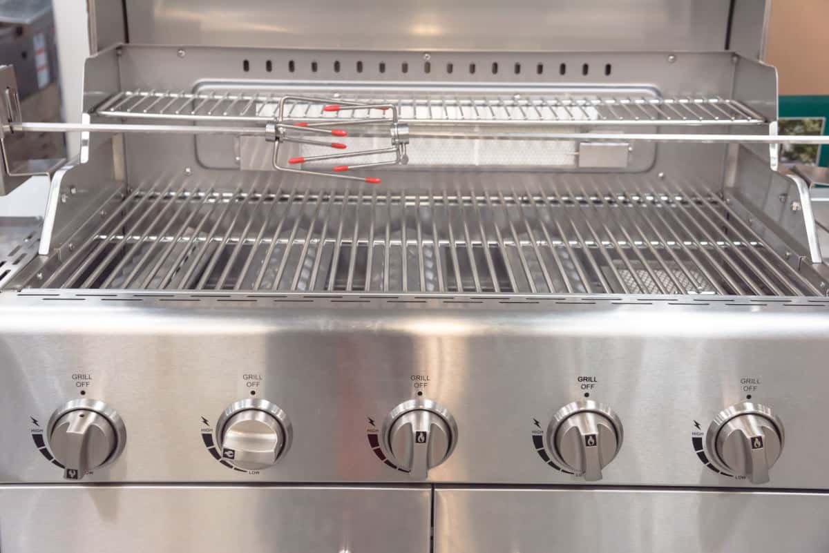 Close up of a gas grill llid open, showing rotisserie attachment