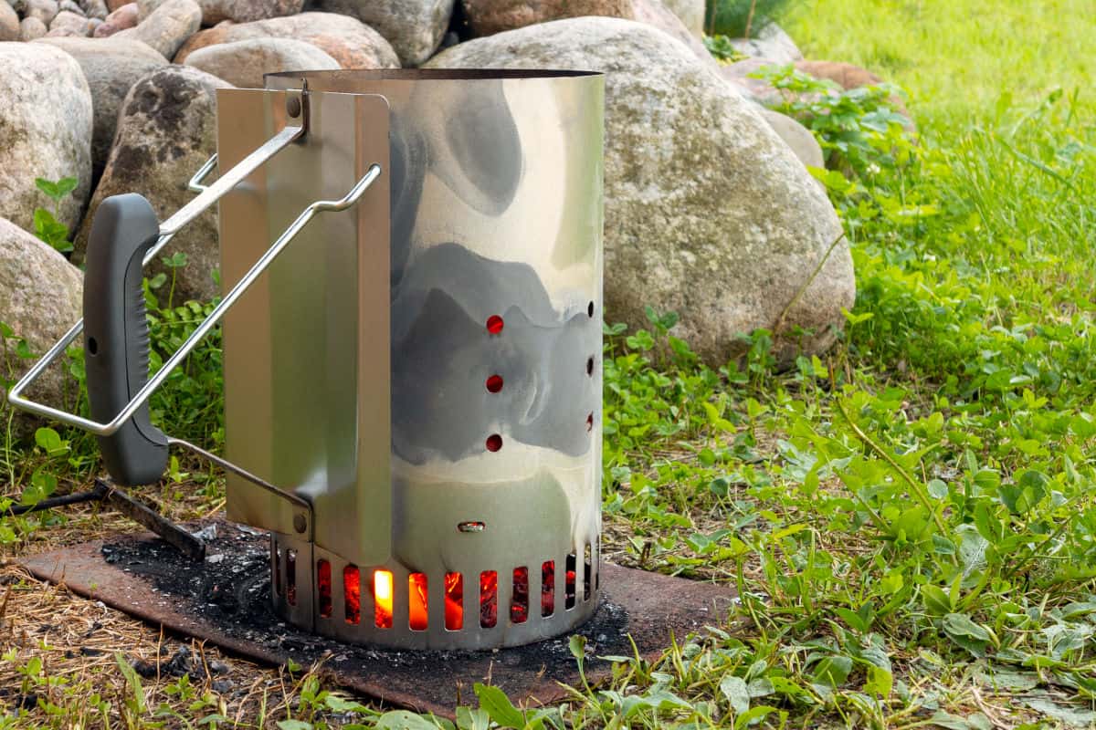 A charcoal chimney starter sat on a metal plate, with paper burning to light the coals