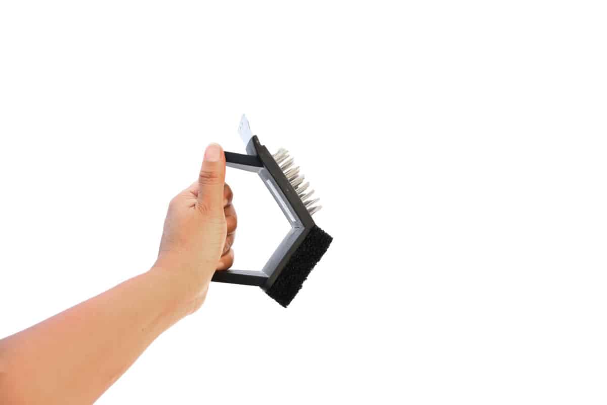 A 3 sided grill brush being held by a man, isolated on white