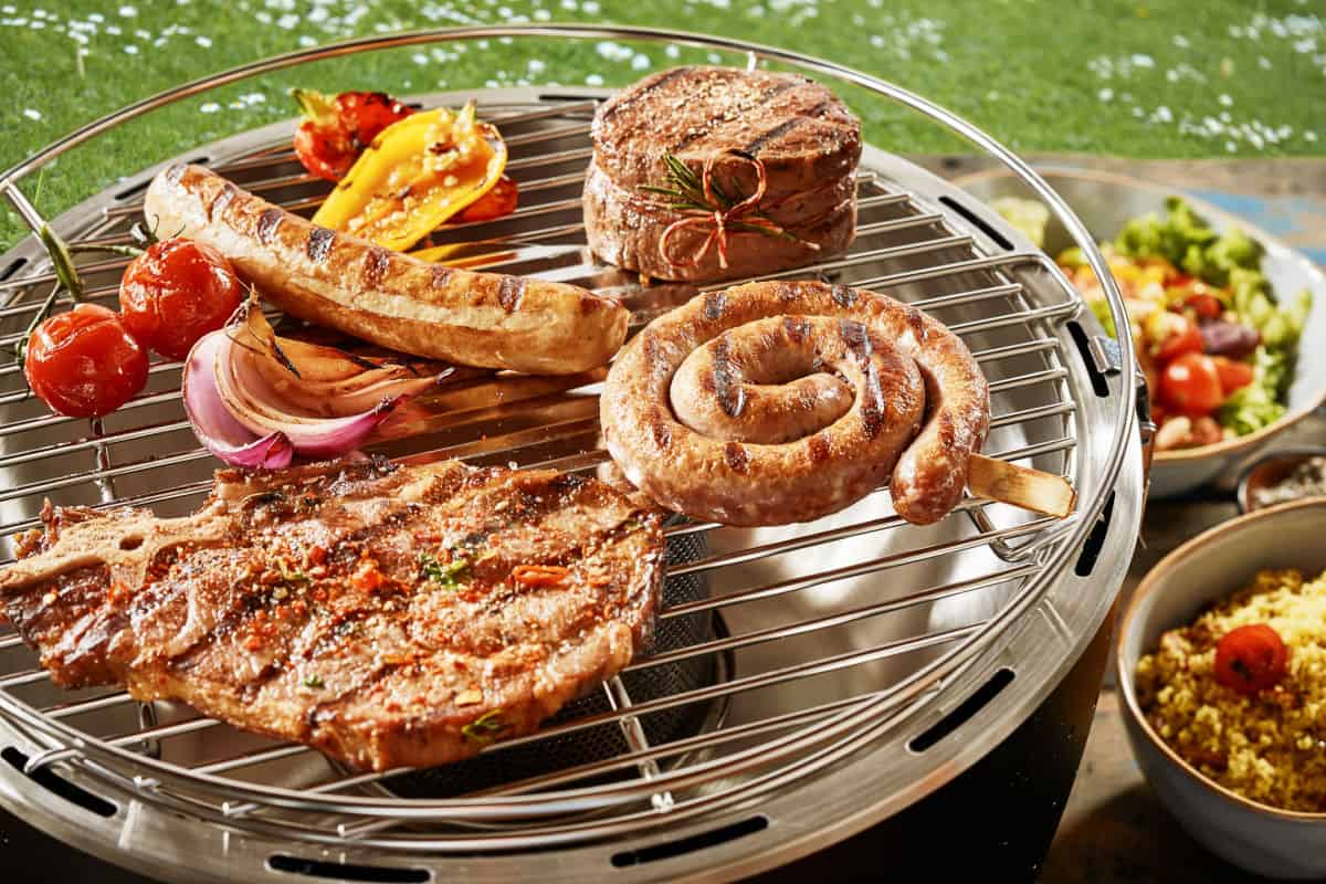 Sausages and steak being grilled on a tabletop gas grill