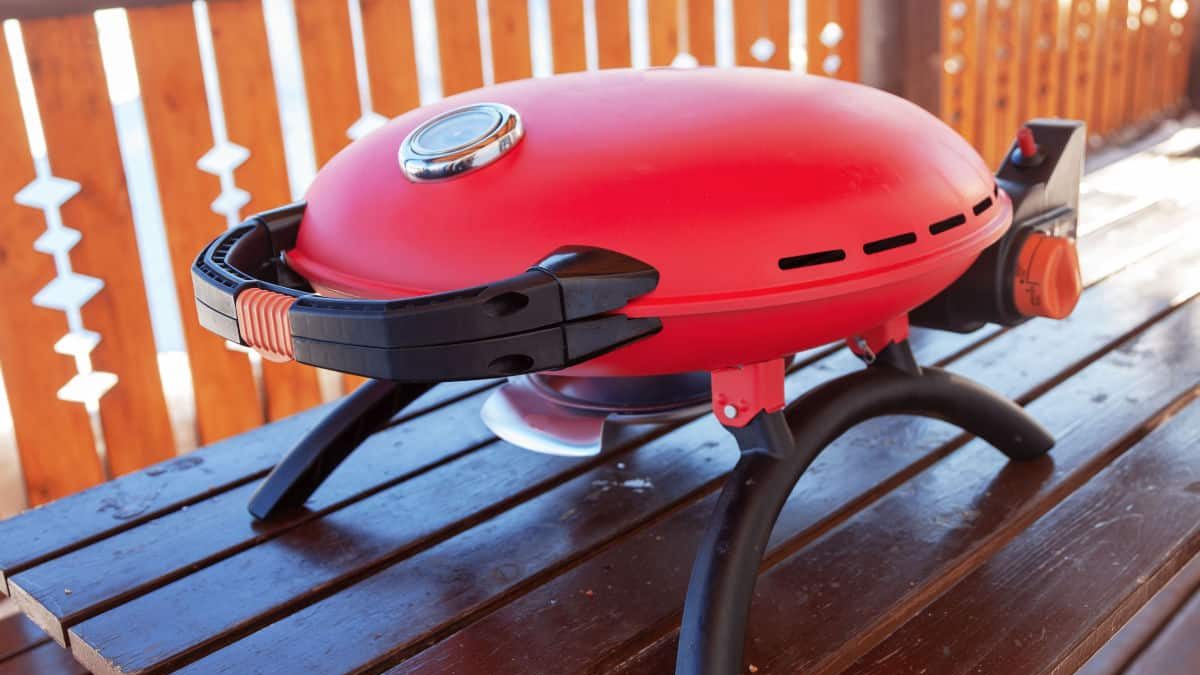A red tabletop gas grill sitting on a wooden table