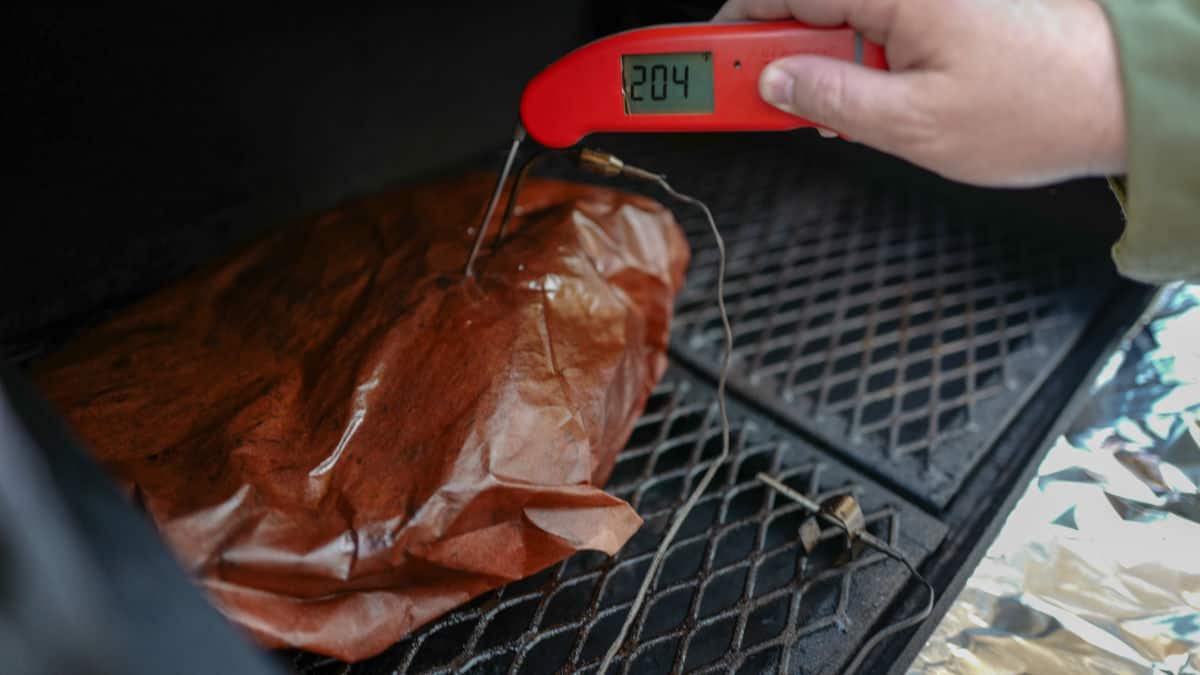 Temp of some meat wrapped in pink butcher paper being taken by an instant read thermometer