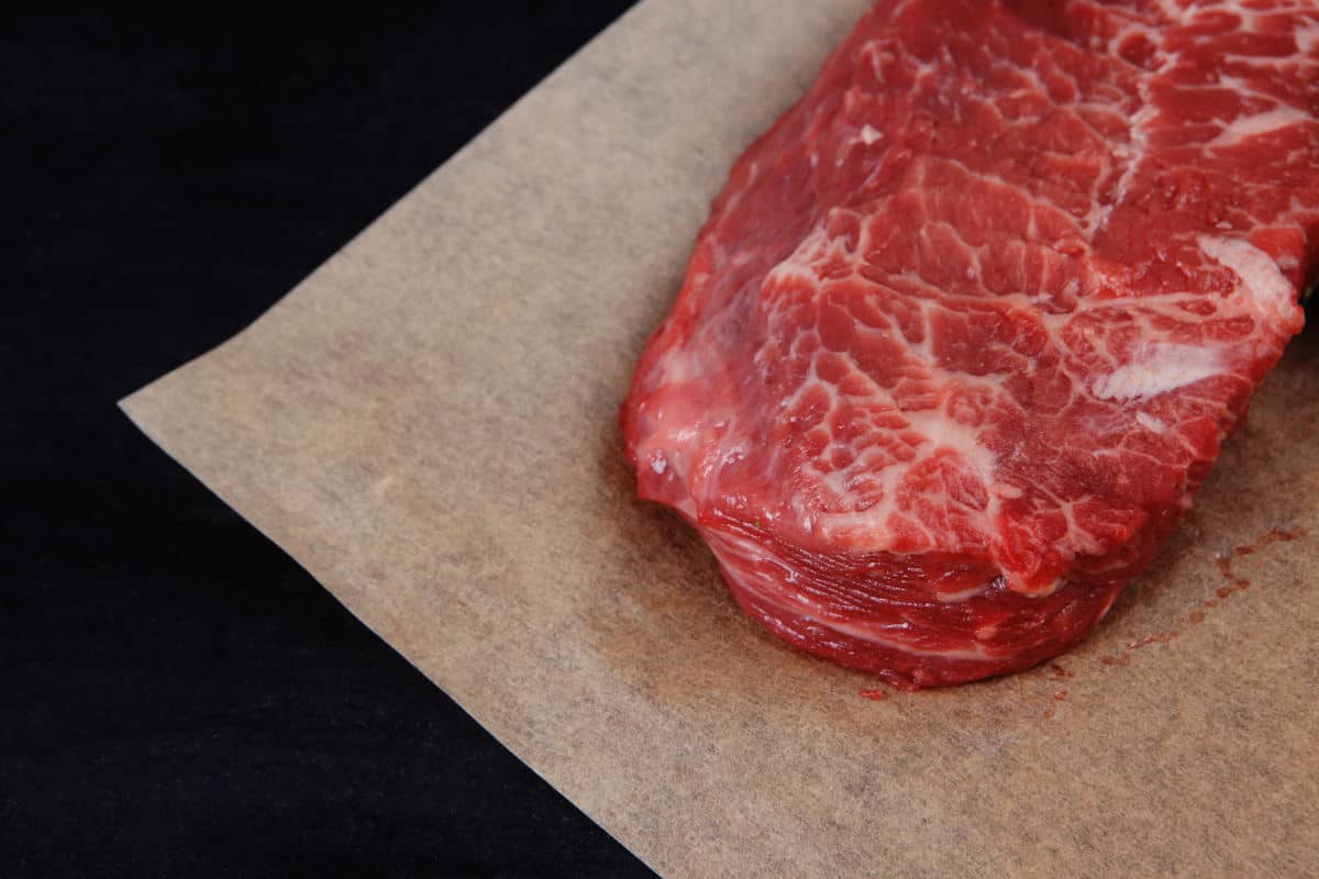 A raw steak sitting on some steak paper on a black surface