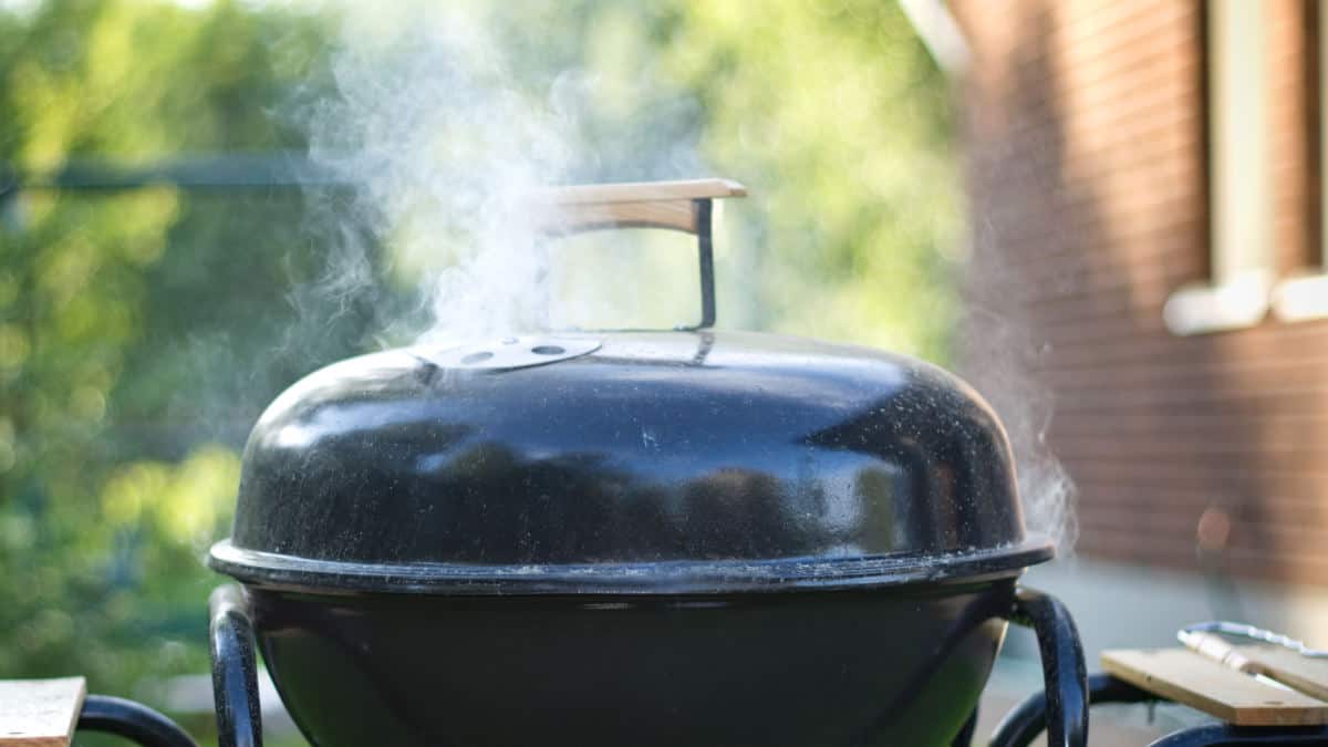 Close up of a charcoal grill, with lid on and smoke billowing from the top vent