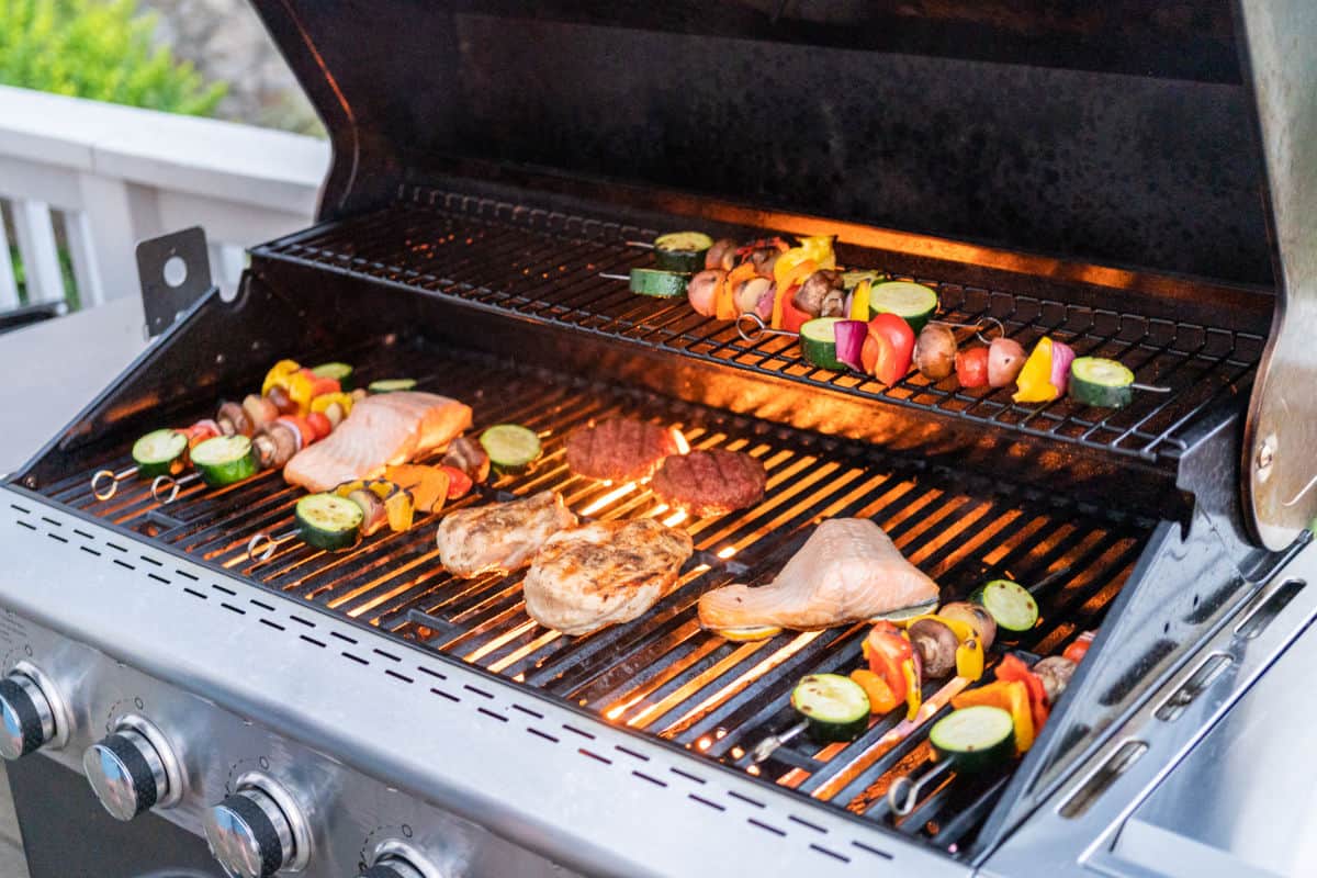 An outdoor gas grill with all burners on, grilling many different meats and kebobs