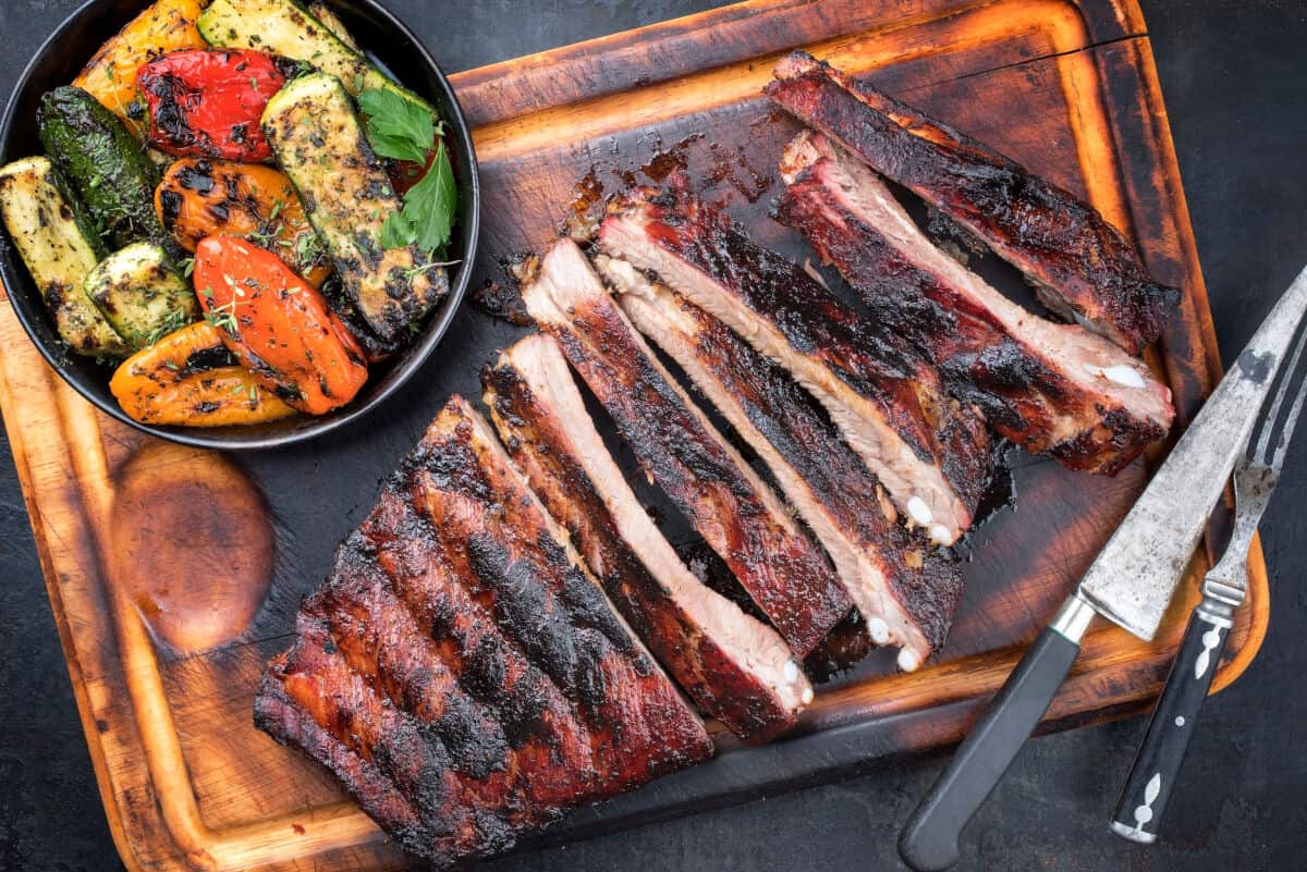 A rack of sliced st louis cut ribs next to a bowl of grilled veg