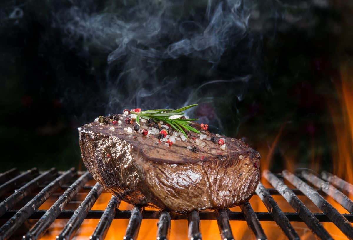 A thick steak on a fiery grill, with a rosemary sprig on top