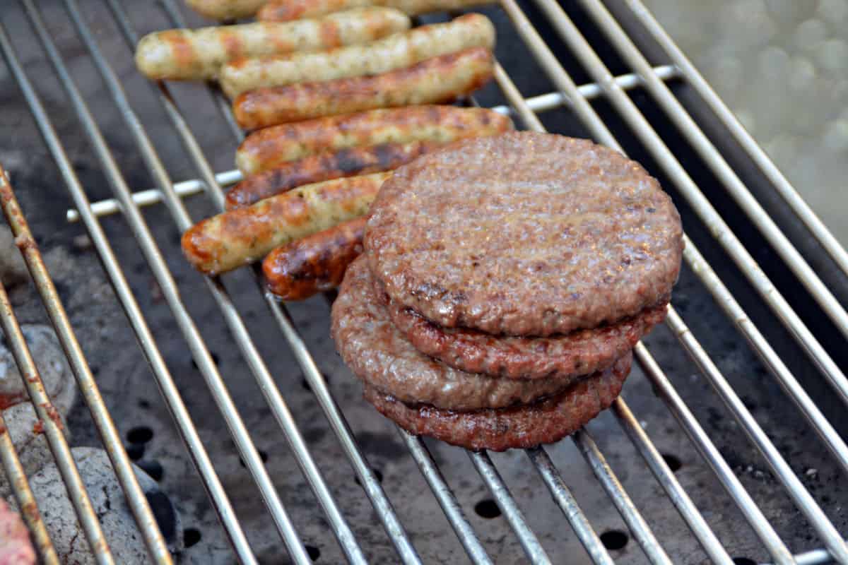 Burgers and sausages being grilled indirect on a charcoal grill