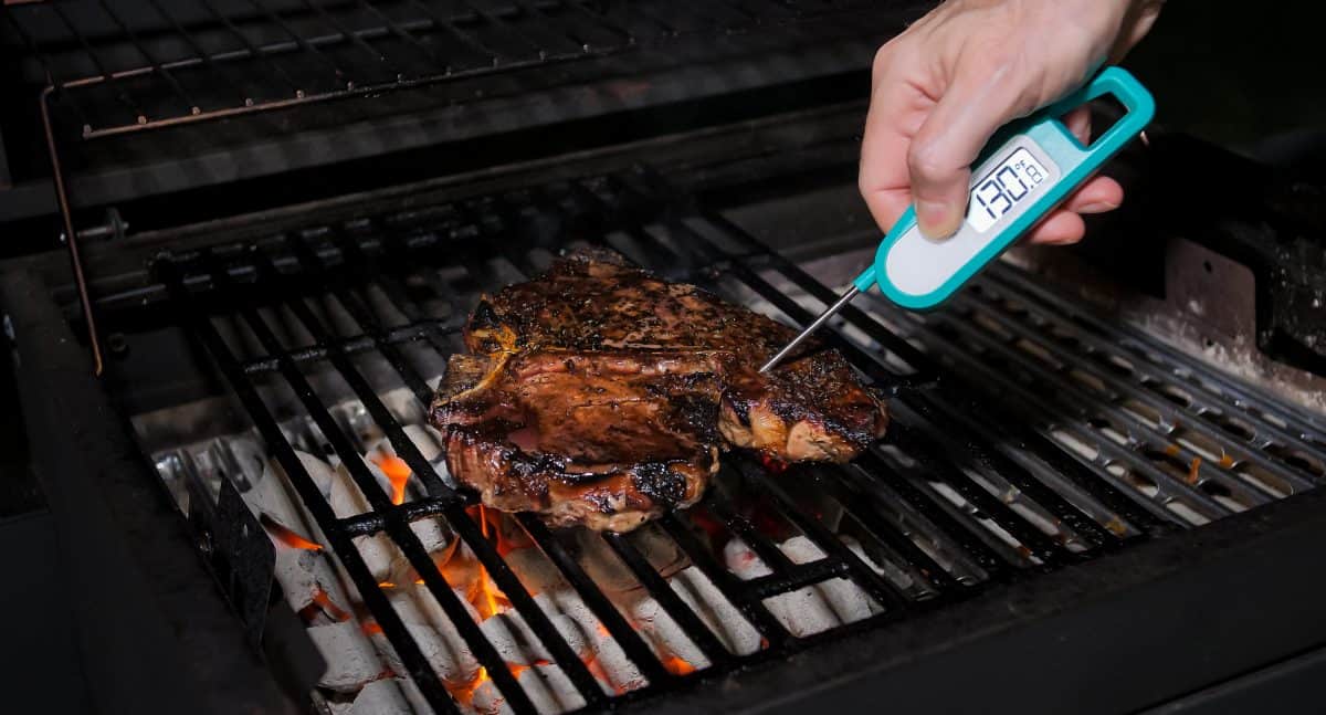 An instant read meat thermometer taking the temperature of a grilling steak
