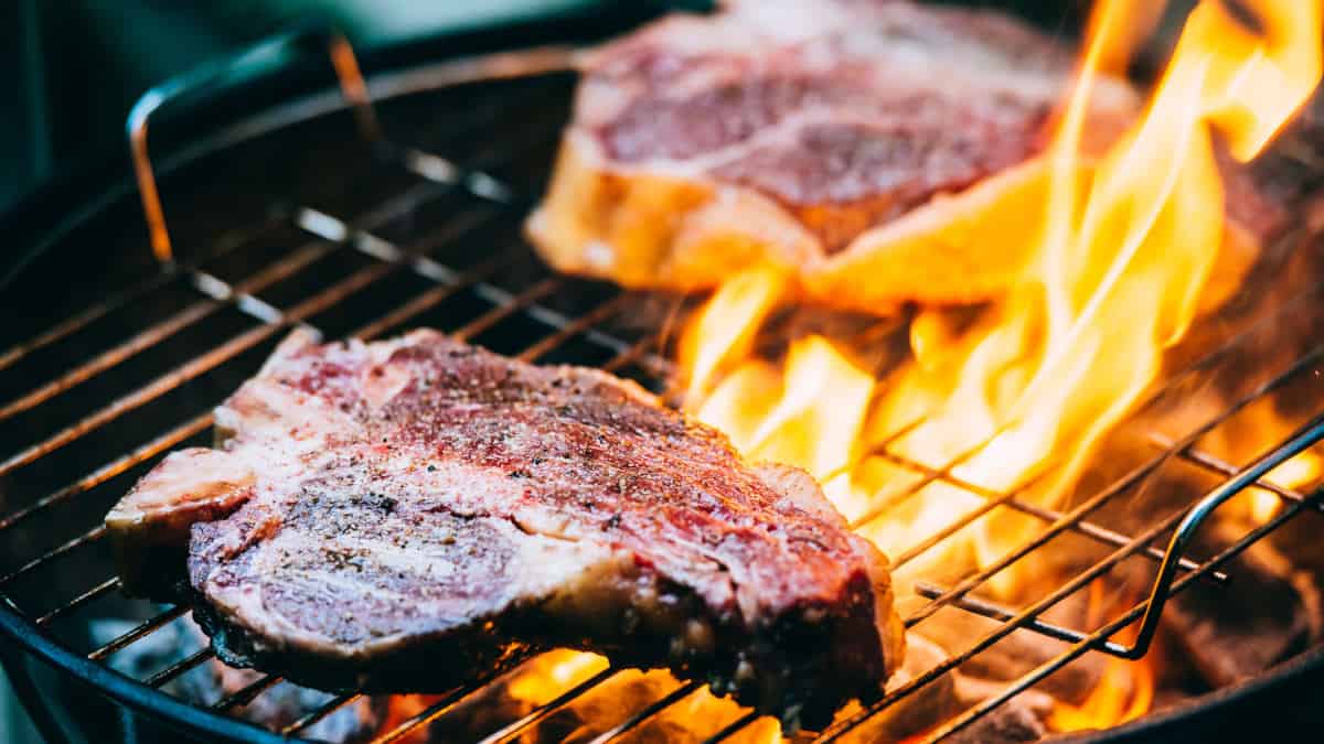 Two t-bone steaks grilling over charcoal