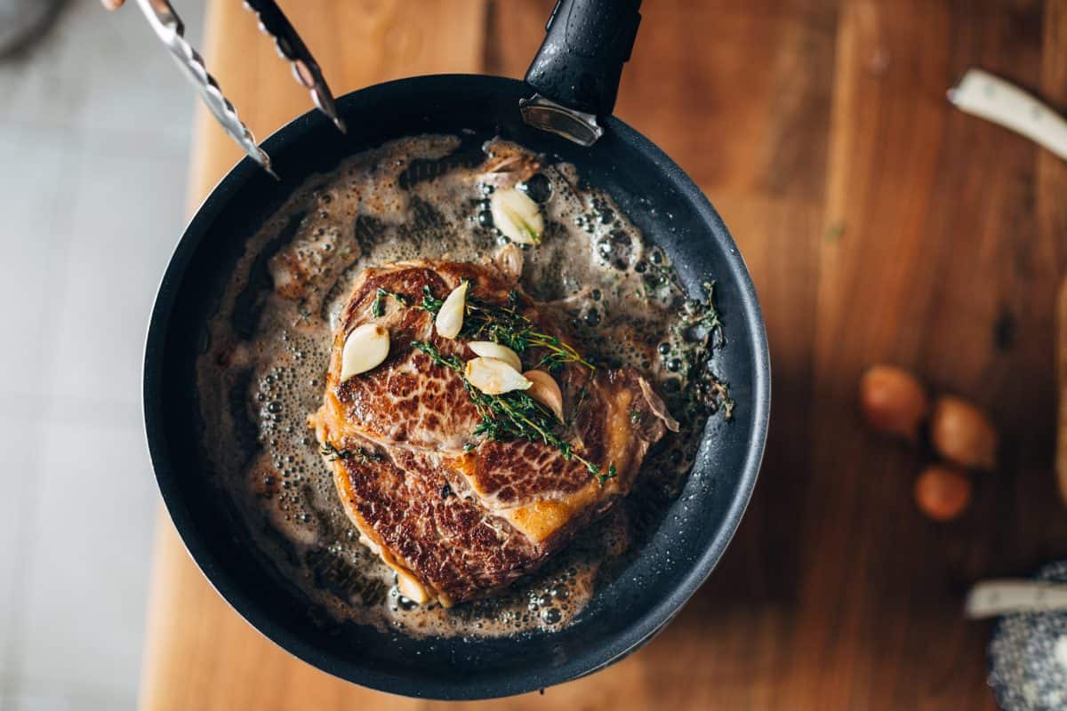 A ribeye steak, frying in a pan with rosemary, garlic and butter