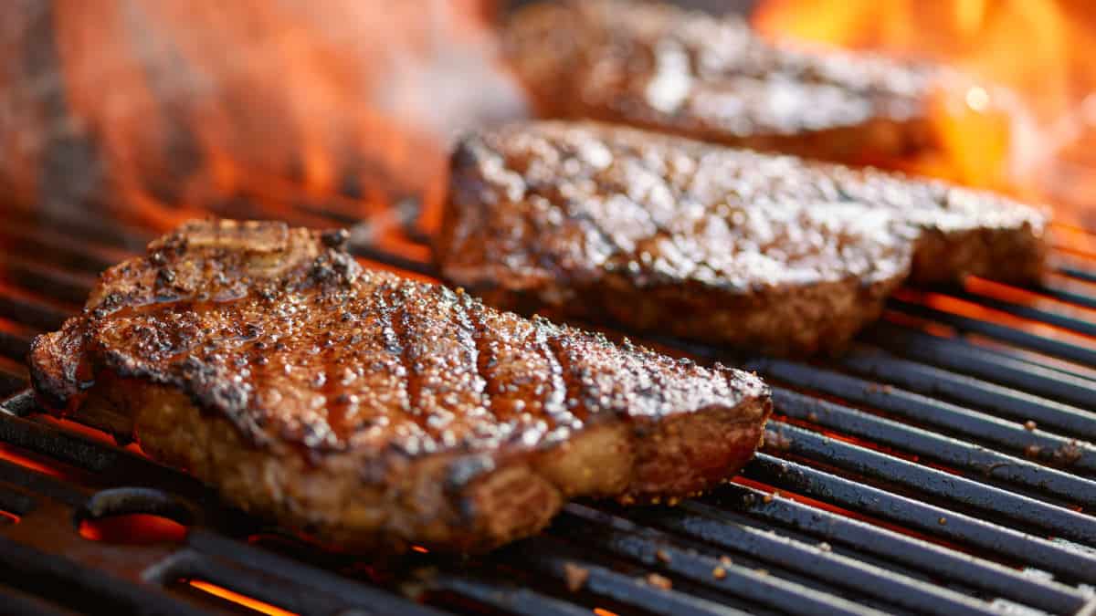 Steaks on a hot grill with flames licking up around the meat