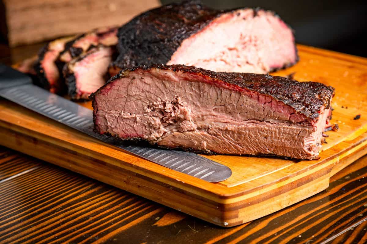 A brisket with smoke ring, cut in half, on a cutting board with a large knife