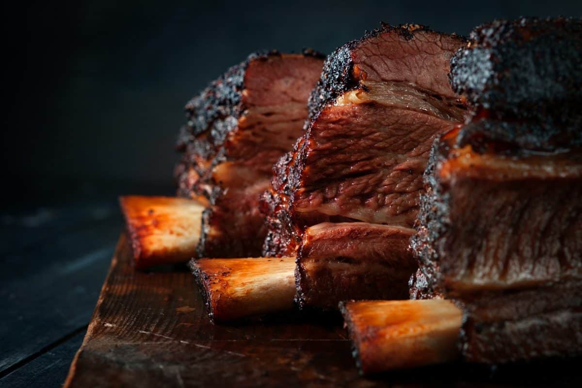 Side view of three smoked beef ribs on a dark background