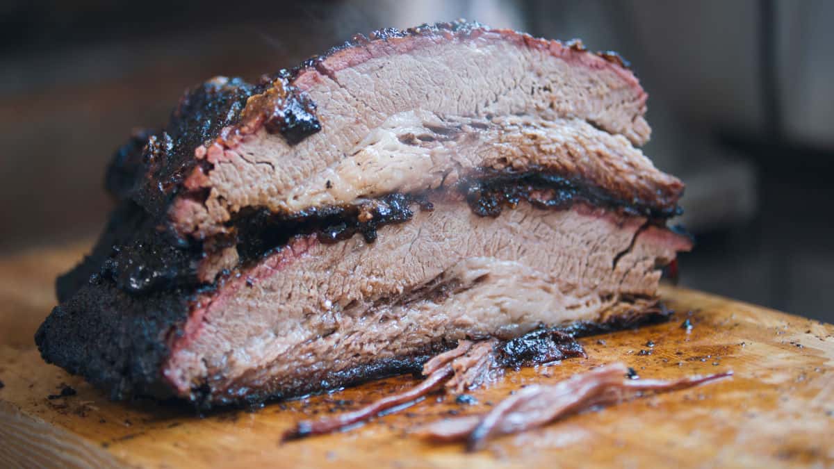 A smoked brisket, cut in half, steaming, on a wooden cutting board