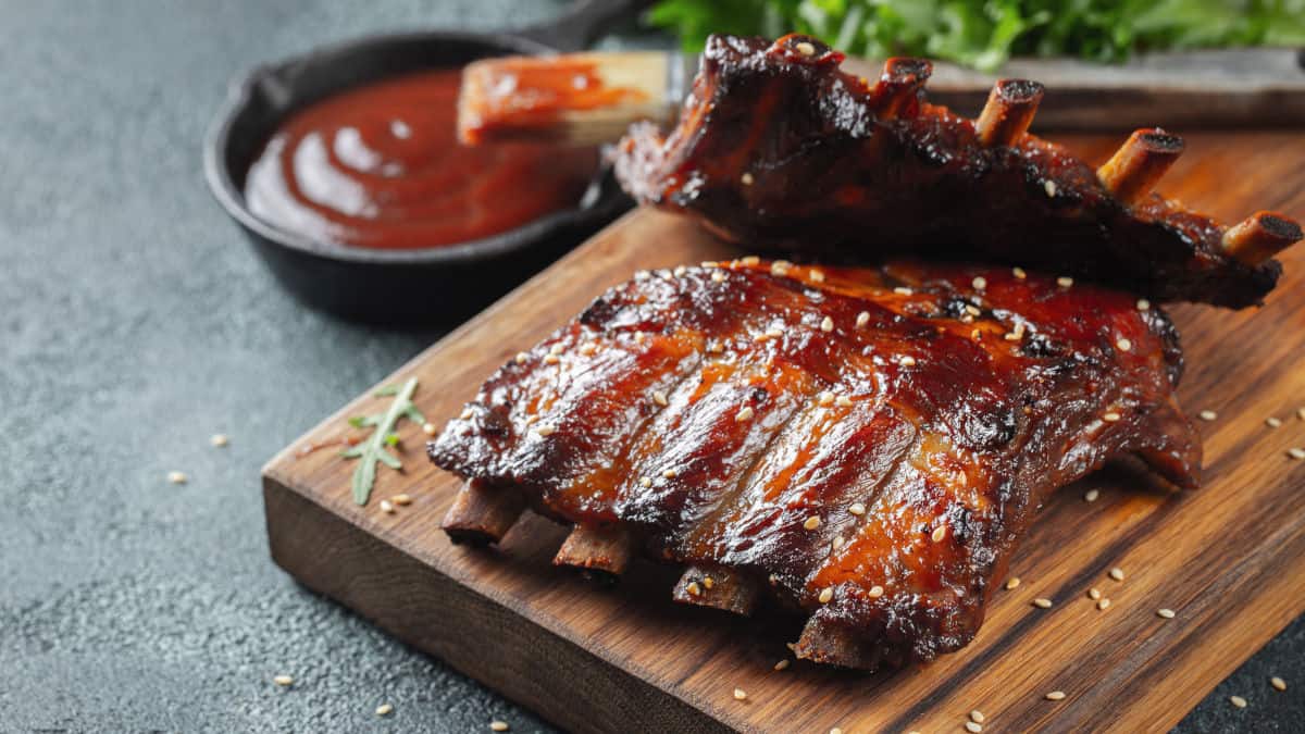 A rack of pork ribs on a cutting board, brushed with sauce