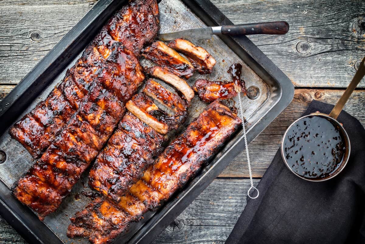 Three racks of pork ribs on a backing sheet brushed with sauce