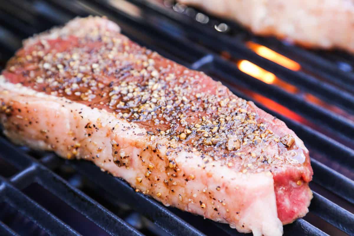 A thick sirloin steak sitting on a charcoal grill grate