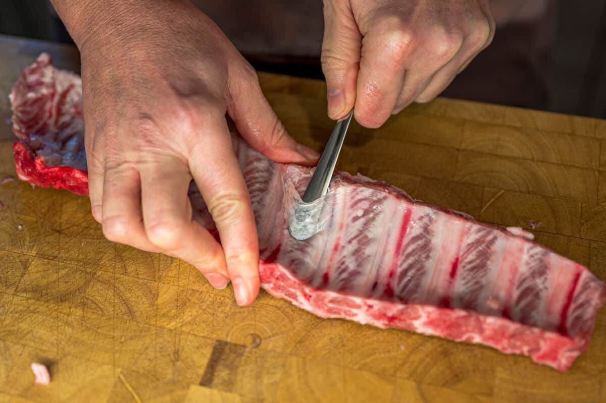 A dull knife being slipped under the skin of a pork rib membrane