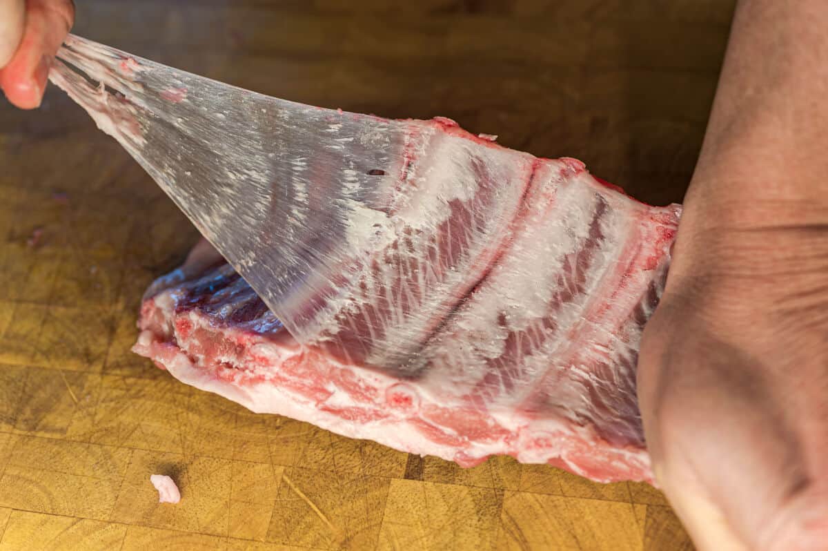 A large piece of membrane being pulled away from a rack of ribs