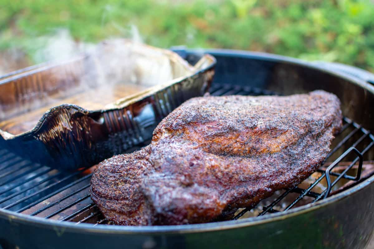 A brisket in a WSM smoker, with water pan beside it